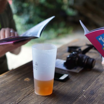 Two people reading London Beer City programmes with a half-drunk pint of beer and a camera on the table